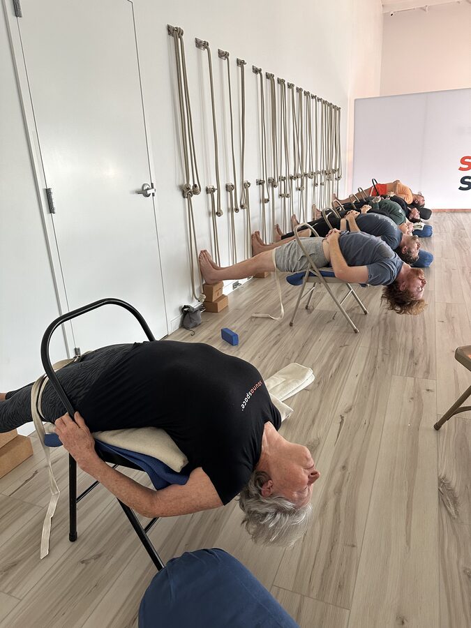Students practicing supported Viparita Dandasana over chairs with props